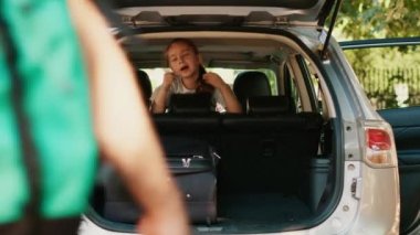 Parents loading voyage luggage inside car trunk while unpatient daughter hurrying them. Casual family going on summer holiday citybreak while loading baggage and trolleys inside vehicle.