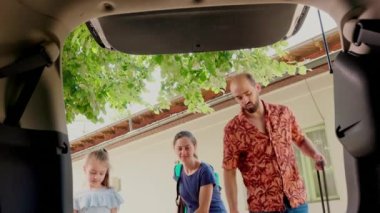 Parents and daughter loading car trunk with trolleys and baggage while getting ready for voyage field trip. Family putting luggage inside vehicle while going on summer holiday journey.