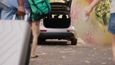 Multiethnic people loading field trip luggage in car trunk while going on summer holiday. Diverse people putting baggage inside vehicle while going on citybreak vacation together.