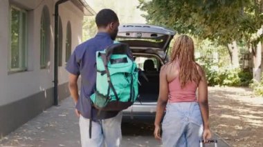 African american couple loading vehicle trunk with voyage luggage while getting ready for holiday citybreak. People putting baggage and trolleys inside car while getting ready for field trip departure