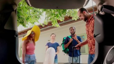 Diverse travellers loading voyage luggage in car trunk while going on summer holiday citybreak. Multiethnic group of friends with baggage and trolleys getting ready for weekend field trip.