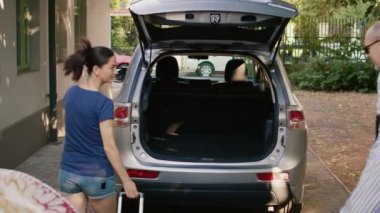 Grandparents with daughter and niece putting voyage baggage in vehicle while going on summer citybreak. Family loading luggage in car trunk while going on holiday field trip.