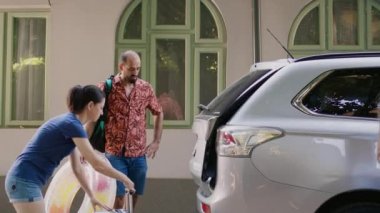 Caucasian family loading voyage luggage in car trunk while getting ready for summer trip departure. Mother and father putting baggage inside vehicle while excited daughter entering automobile.