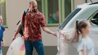 Positive family loading holiday baggage and trolleys inside car trunk while going on summer citybreak. Daughter and parents getting ready for summer vacation while putting luggage inside vehicle.