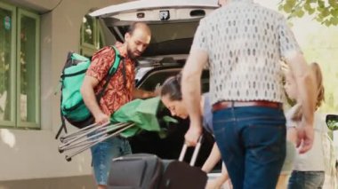 Family loading voyage baggage and trolleys inside car trunk while going on summer vacation citybreak. Casual people going on holiday field trip while putting luggage inside vehicle.