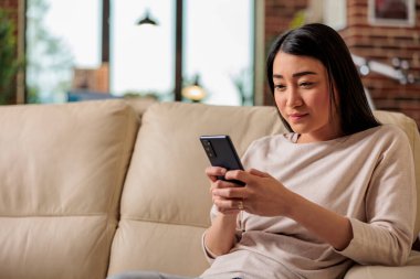 Normal görünümlü mutlu Asyalı kadın evde akıllı telefon kullanıyor, internet teknolojisi akıllı telefon kullanıcısı cep telefonu kullanıcı cep telefonu sosyal medya iletişim dijital aygıtı