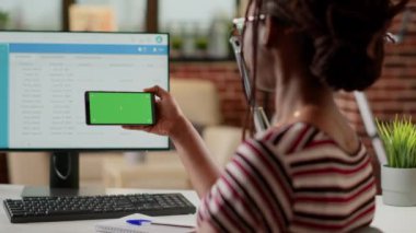 Woman using horizontal greenscreen on smartphone, sitting at desk. Freelancer looking at blank mockup background with isolated copyspace and chroma key template on telephone display.