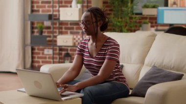 Female freelancer browsing internet on laptop to do remote work on couch. Business student working remotely on computer, analyzing startup research with online network from home.