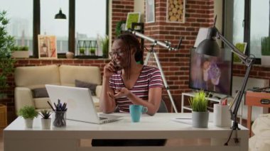 Female freelancer answering phone call on smartphone, working remotely on laptop from home. Student woman doing remote telecommunications job and talking on telephone line at desk.