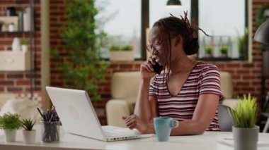 Woman freelancer answering phone call at remote job, working from home and talking to manager on smartphone. Using telephone line to chat remotely, telecommunications network at desk.