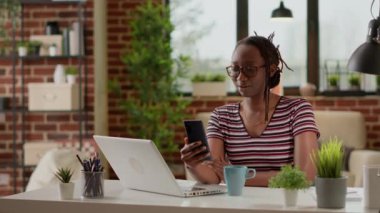 Freelancer using online videoconference call to talk to colleagues and do remote work on smartphone. Young woman talking on virtual internet teleconference, using computer webcam.