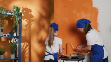 Woman with small girl doing housework improvement to change walls color in apartment. People using paintbrush, roller tools and diy equipment to renovate house interior and redecorate. Tripod shot.
