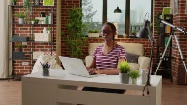 Portrait of female employee working remotely from home, using laptop and online connection to do business job in living room. Office worker doing startup remote work at desk.