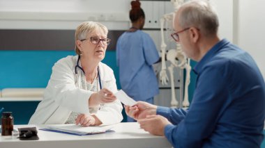 Medic writing checkup information on prescription paper to give treatment medicine to retired person at medical appointment. Taking notes on consultation report, diagnosis results.