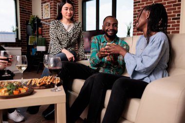 Interracial people enjoying time together while giving each other gifts and drinking alcoholic beverages. Diverse group of friends celebrating birthday at wine party while exchaning gifts.