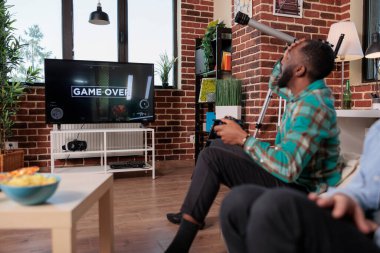 Young adult feeling frustrated about lost video games competition, playing shooting game on tv console and losing. Sad man being angry after gaming strategy lose, relaxing with friends.
