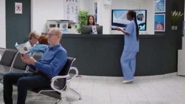 African american nurse talking to asian receptionist at hospital reception counter, discussing about checkup appointments and patient treatment. Healthcare worker at medical facility.
