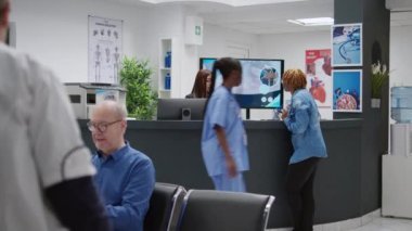 African american woman using credit card to pay medical visit appointment, paying consultation and treatment at hospital reception counter. Patient talking to receptionist in waiting area lobby.