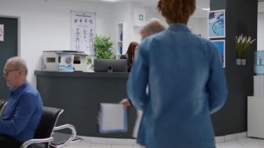 Medical worker helping with appointments at hospital reception desk in facility waiting room, giving clinical support. Receptionist working at healthcare center counter with checkup report.