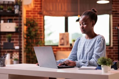 Successful corporate remote worker writing on laptop and working in modern home office. Smiling female freelancer using portable computer in contemporary coprorate workspace