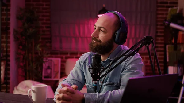 Online radio talk show host pausing conversation with guest to answer live call from listener in home studio. Closeup of man recording podcast using professional audio equipment and microphone.