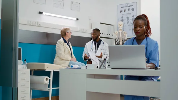 Diverse people doing medical consultation in clinical office, attending checkup visit appointment with facility staff. Doctor and patient talking about medicine and healthcare at examination.