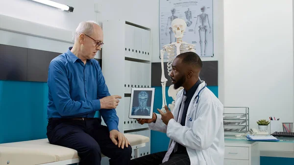 Medic physician explaining x ray scan results to patient in medical cabinet, analyzing bones radiography diagnosis on digital tablet to give treatment. Healthcare checkup appointment with doctor.