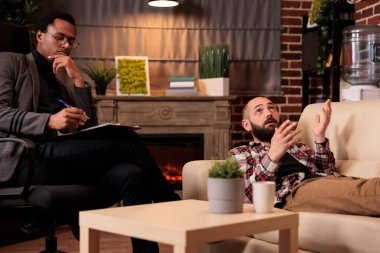 African american psychologist consulting man laying on couch, doing psychoanalysis to solve problems at therapy session. Talking about behavior issues and giving counseling advice.