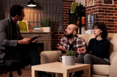 Young couple trying to solve relationship problems with professional psychologist at therapy session. Giving counseling advice and support, feeling happy about reconciliation and holding hands.