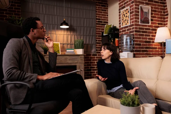 Female patient laying on sofa at psychotherapy session with therapist, talking about stress and problems. Receiving support and help from professional counselor, behavior guidance.