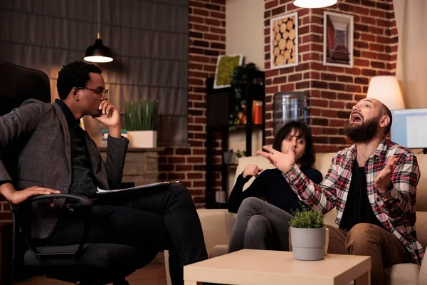 Male psychotherapist doing psychoanalysis of people at couple therapy, trying to solve relationship difficulties at counseling session. Angry man talking about fight and conflict, find solution.