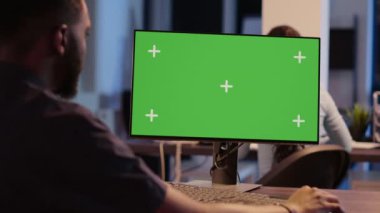 African american man looking at computer with greenscreen, analyzing isolated display on desktop monitor. Using blank copyspace template with mockup screen and chroma key background.