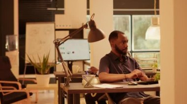 Corporate employee leaving office and waving at colleague, working on business presentation report with data research. Using network information on computer to plan startup project.