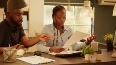 African american team of business people working with documents to plan research presentation and do management report. Doing teamwork analyzing paperwork and data notes during sunset.