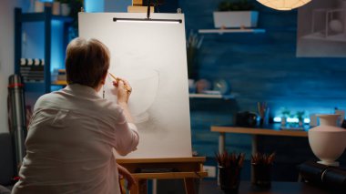 Emeklilik yaşında kadın sanatçı tuval üzerine vazo çizmek için kalem kullanıyor ve sanatsal becerileri olan profesyonel bir başyapıt yaratıyor. Sanat ve zanaat araçları ile otantik çizim modeli çiziliyor.