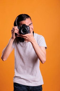 Photographer taking photos on professional digital camera, looking in viewfinder. Young asian man using photographing equipment, front view medium shot, creative hobby, photoshoot