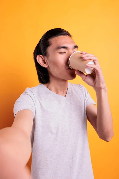 Young man talking on video chat, drinking coffee first person view. Asian teenager chatting on mobile phone videoconference, enjoying take away tea fpv, online meeting pov