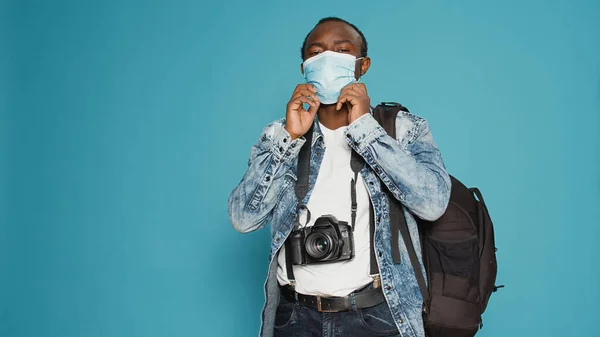 Adult photographer putting face mask on to leave on vacation trip, using camera to take pictures and capture urban adventure during covid 19 pandemic. Taking photos with equipment.