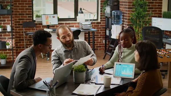 Diverse team of coworkers analyzing business charts on documents, working on presentation report in boardroom. Using data on documents to plan research in corporate management meeting.