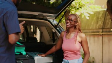 Beautiful woman discussing with boyfriend about holiday field trip beside trunk full of luggage. Couple talking about summer citybreak plan while getting ready for vacation departure.