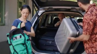 Family getting ready for summer field trip while loading vehicle with voyage trolleys and citybreak. Parents putting luggage in car trunk while unpatient daughter hurrying them.