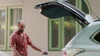Positive family loading car trunk with voyage trolleys and luggage while going on holiday summer citybreak. Parents and daughter getting ready for beach trip while putting baggage inside vehicle.