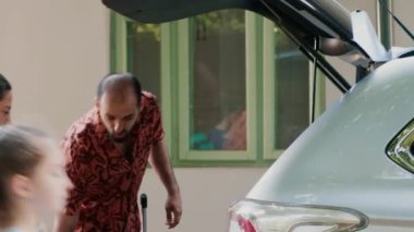 Parents and daughter getting ready for beach trip while putting baggage inside vehicle. Positive family loading car trunk with voyage trolleys and luggage while going on holiday summer citybreak.