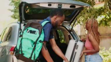 African american couple loading voyage luggage and trolleys inside car trunk while getting ready for holiday citybreak departure. People putting baggage inside vehicle while going on field trip.