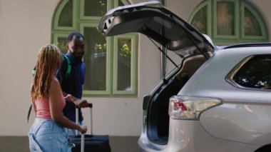 Boyfriend and girlfriend putting baggage and trolleys in vehicle trunk. African american couple loading voyage luggage in car while getting ready for summer citybreak departure.