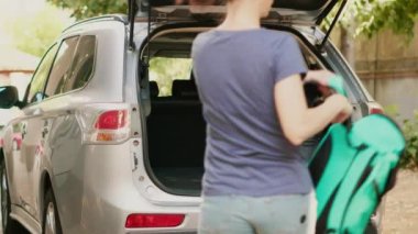 Mother and daughter going on summer holiday with african american family friend while loading luggage in car trunk. Multiethnic people putting baggage inside vehicle while getting ready for citybreak.