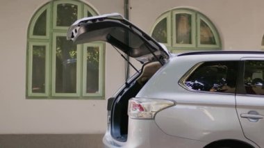 Positive people putting baggage and trolleys inside vehicle while going on field trip. Big family loading voyage luggage in vehicle trunk while getting ready for summer citybreak departure.