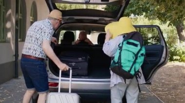 Grandparents loading car trunk with luggage while unpatient granddaughter hurrying them. Senior couple and niece going on summer field trip while putting voyage baggage and trolleys in vehicle
