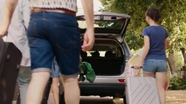 Big family loading voyage baggage in vehicle trunk while preparing for field trip departure. People putting luggage and trolleys inside car while getting ready for citybreak departure.