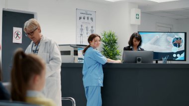Hastane resepsiyonunda çalışan, lobi masasına yaslanmış tıbbi asistanın portresi. Sağlık hizmetleri kliniğindeki bekleme odasında hemşire, tesiste check-up randevusu. El kamerasıyla..